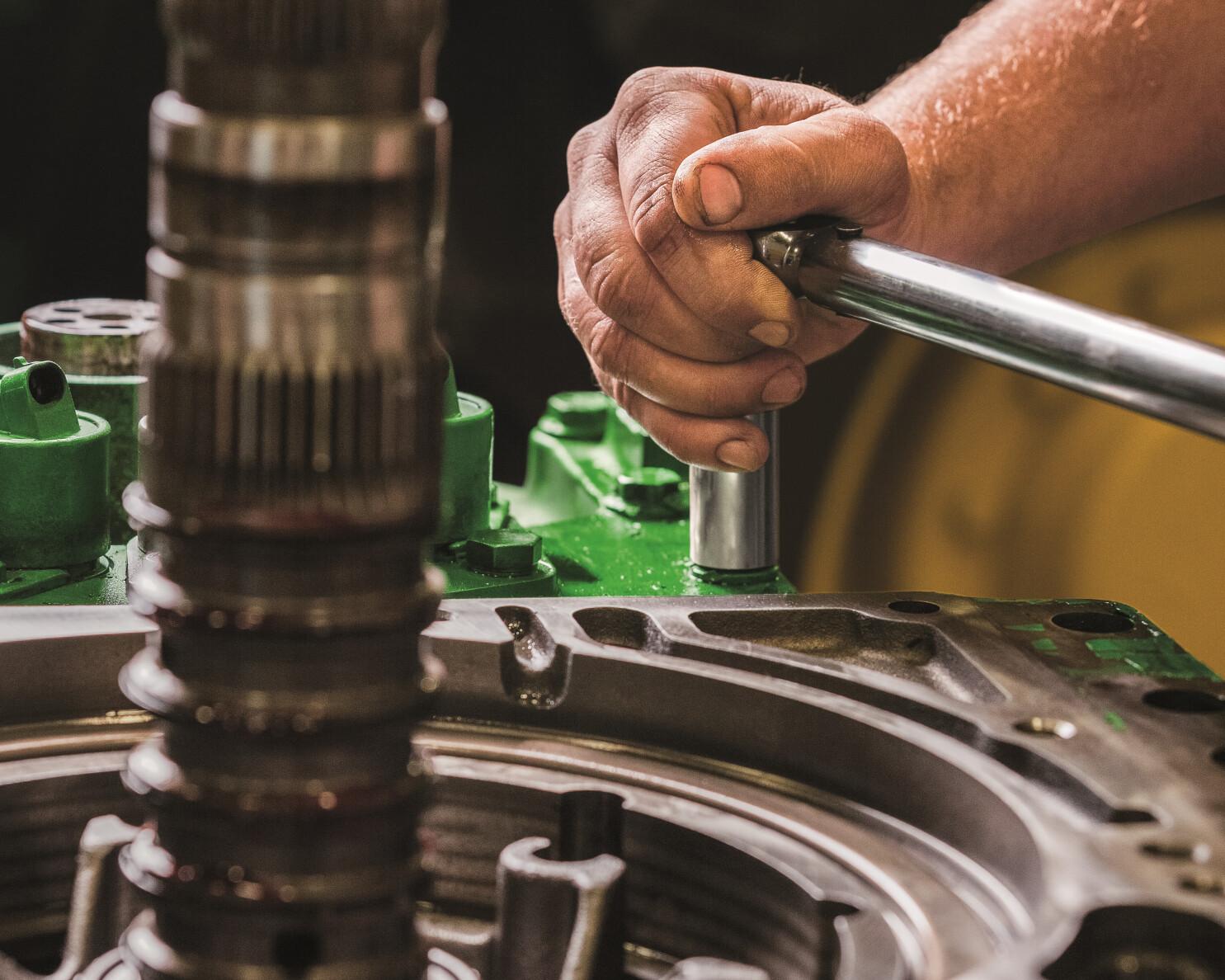 A service worker tightens a bolt on a John Deere tractor.