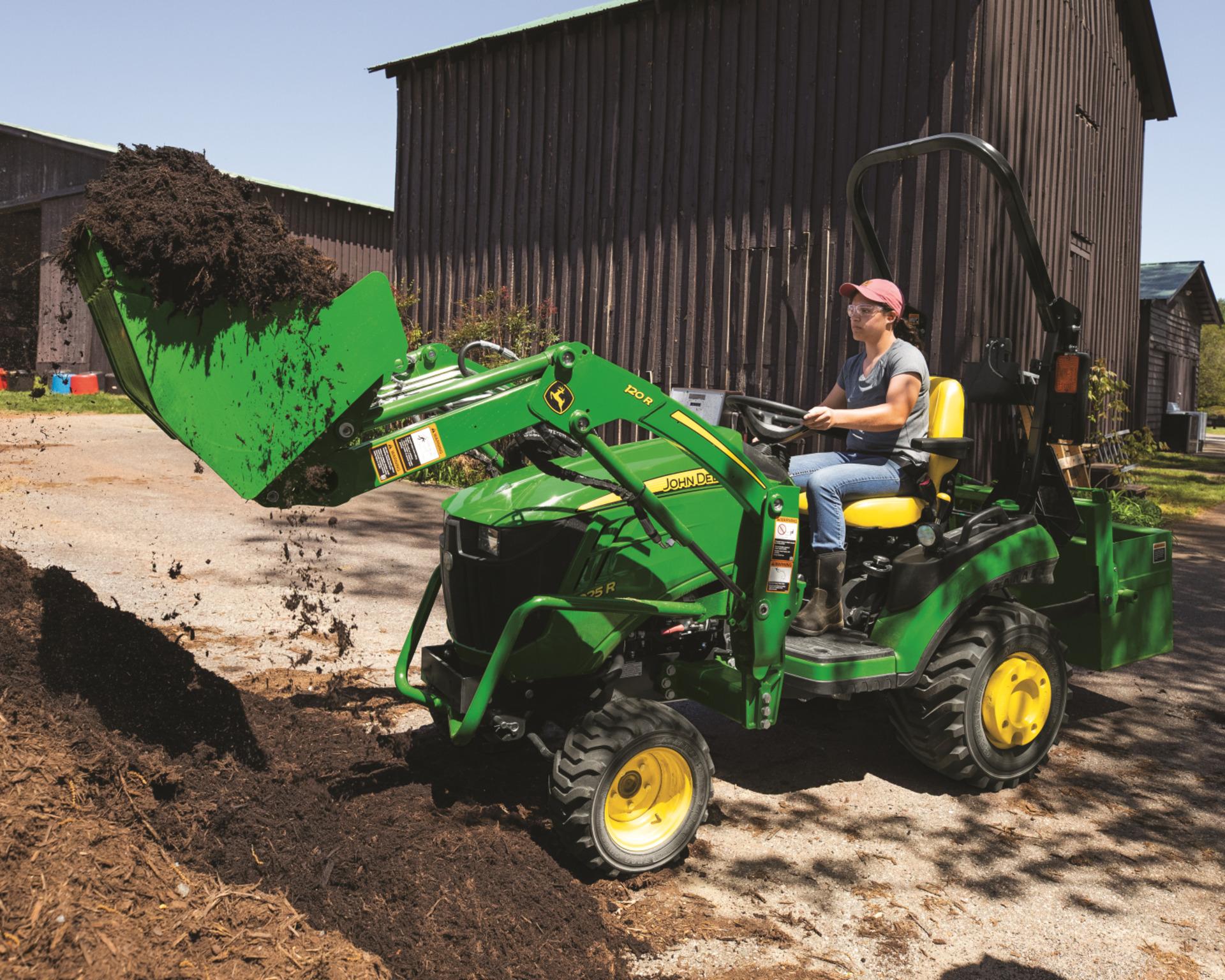 A John Deere 1025R with a front-end loader attachment lifting soil.