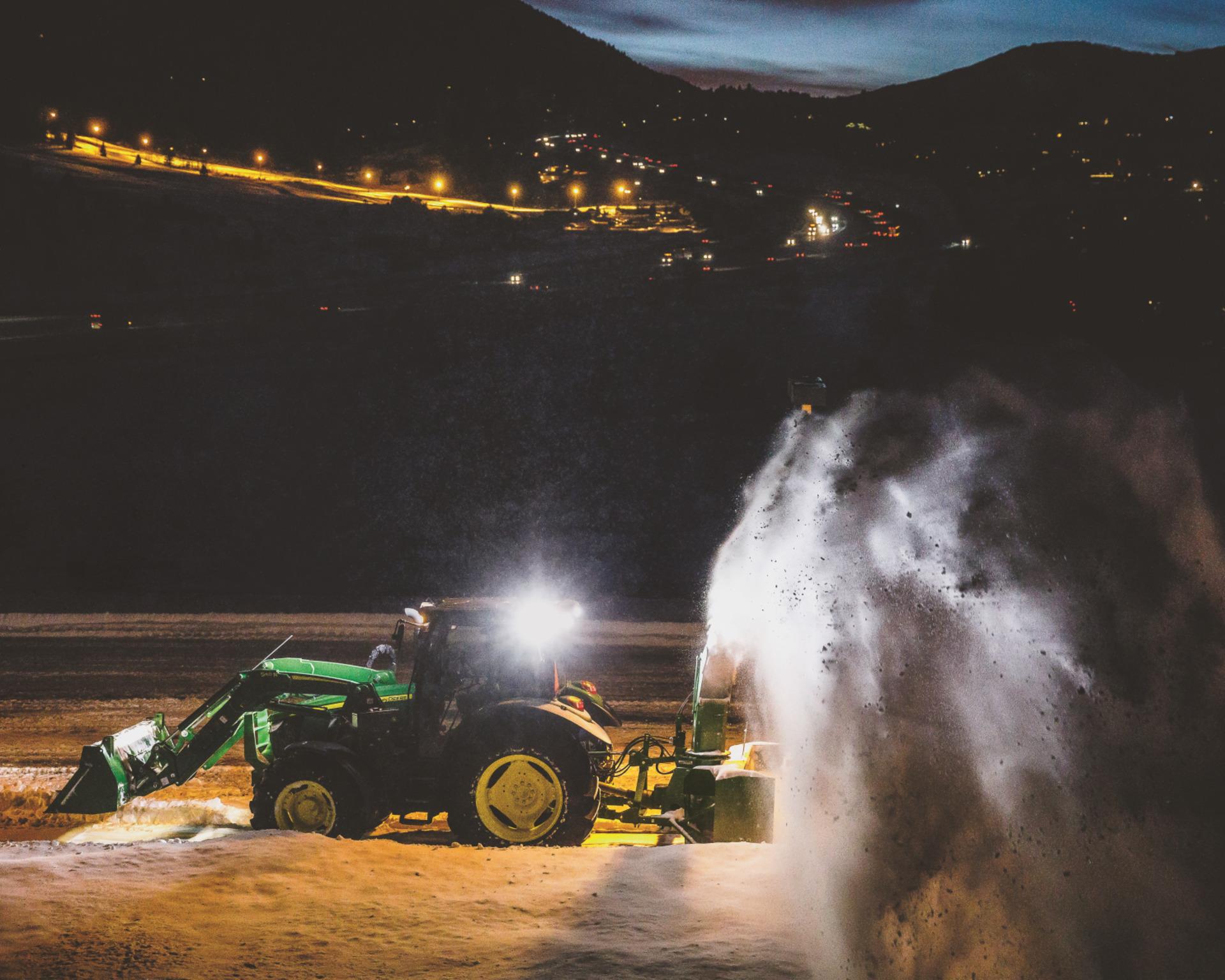 A John Deere snow blower attachment on a compact utility tractor.